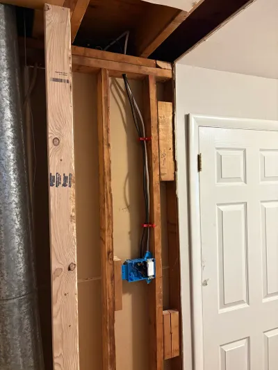 Open basement wall framing with exposed studs and electrical rough-in wiring next to a finished white door.