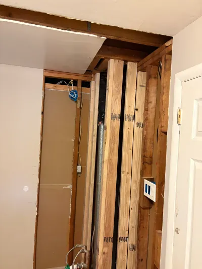 Basement closet wall opened to expose wood framing, wiring, and a plumbing shut-off valve during renovation.