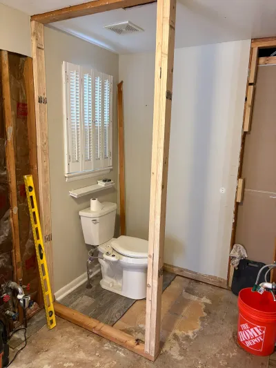 Bathroom under renovation with new stud framing, exposed insulation, and toilet still in place.