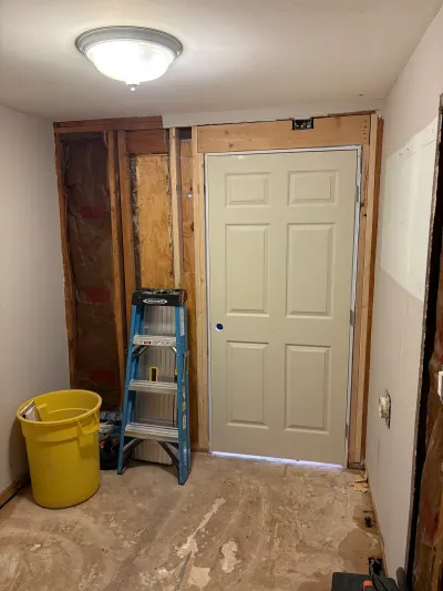An entryway mid-renovation with a new exterior door installed and surrounding wall framing exposed.