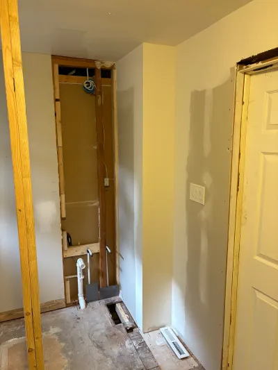 Bathroom under renovation showing exposed stud framing, rough plumbing, and a partially finished wall.