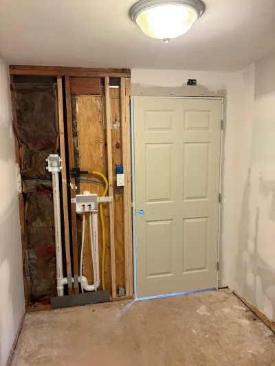 Laundry closet mid-renovation with exposed studs, rough-in plumbing and gas line, and a finished door.