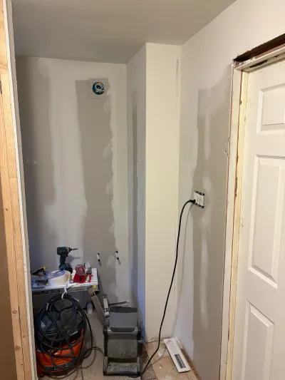 A small closet under construction with taped drywall, exposed framing, and renovation tools on the floor.
