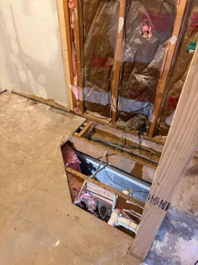 Open wall and floor framing during renovation showing insulation, wiring, and plumbing rough-in.