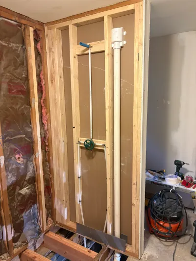 Basement under construction with exposed studs, rough-in plumbing, and a cut-open subfloor.
