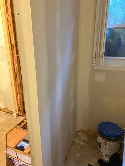 Bathroom mid-renovation with taped drywall, exposed subfloor and framing, and a window.