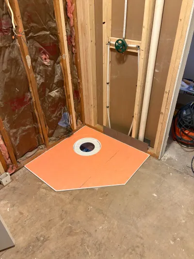 Basement shower rough-in with orange waterproofing pan, exposed studs, insulation, and plumbing lines.