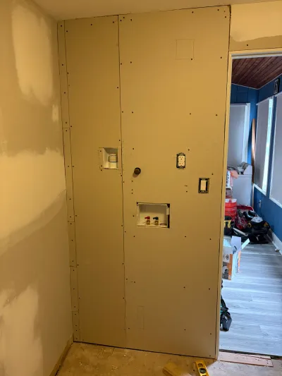 Bathroom mid-renovation with hung drywall, rough-in plumbing and electrical, and subfloor exposed.