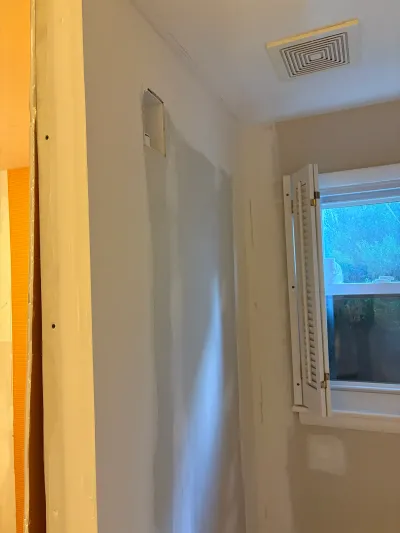 Bathroom mid-renovation with sanded drywall, an exhaust fan vent, and a shuttered window.