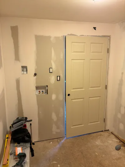 A laundry room mid-renovation with taped drywall, a rough-in laundry box, and a newly hung door.