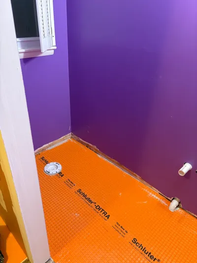 Bathroom mid-renovation with orange tile underlayment on the floor and bright purple walls.