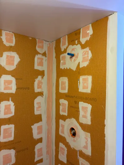 Shower walls covered in waterproof cement board with taped seams before tile installation.