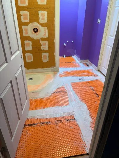 Bathroom mid-renovation with orange Ditra membrane flooring and Kerdi-Board shower wall prep against purple walls.
