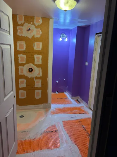 Bathroom mid-renovation with waterproofing membrane on shower walls and floor, purple painted walls.