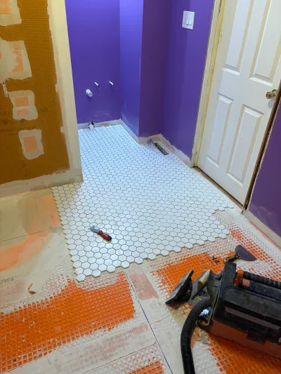 Bathroom floor mid-installation with white hexagon tile over waterproofing membrane and purple walls.