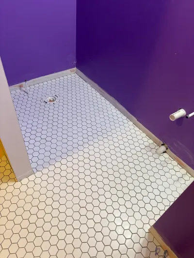 Bathroom mid-renovation with new white hexagon tile floor, plumbing rough-in, and purple walls.