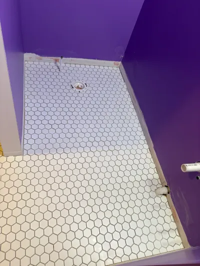 White hexagon tile flooring mid-installation in a bathroom with exposed toilet flange and plumbing.