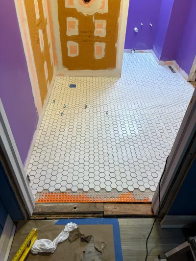 Bathroom renovation in progress with white hex tile flooring and waterproofed shower walls.