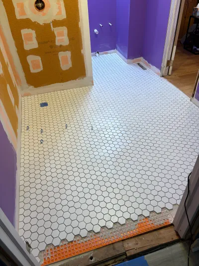 Bathroom floor mid-renovation with white hexagon tile freshly laid and waterproofing membrane on the wall.