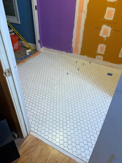 Bathroom mid-renovation with new white hexagon tile floor and waterproofing membrane on the wall.