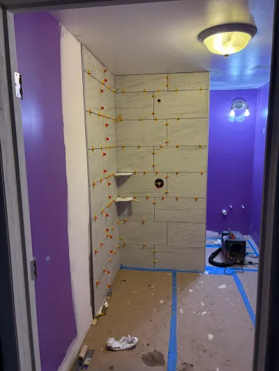 A shower under renovation with newly tiled walls, exposed spacers, and a purple-painted surrounding bathroom.
