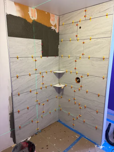 A shower stall under construction with porcelain tile partially installed and leveling clips still in place.