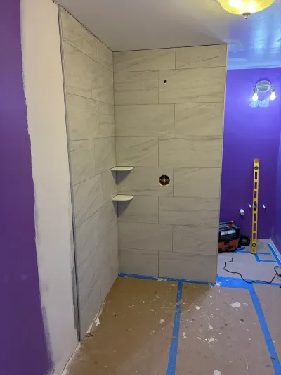 A newly tiled shower stall under construction, with rough plumbing holes and a purple accent wall in the background.