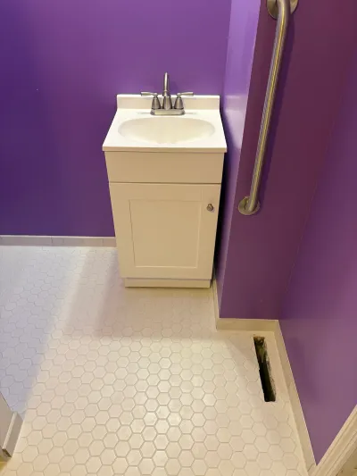 Small bathroom with a white shaker vanity, purple walls, and white hexagon tile flooring.