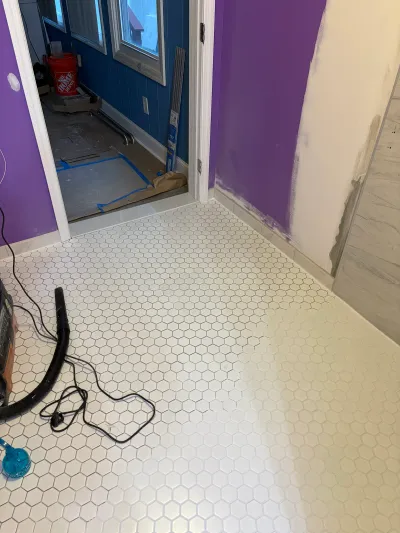 Bathroom mid-renovation with new hex tile flooring, purple walls being primed, and materials staged for installation.