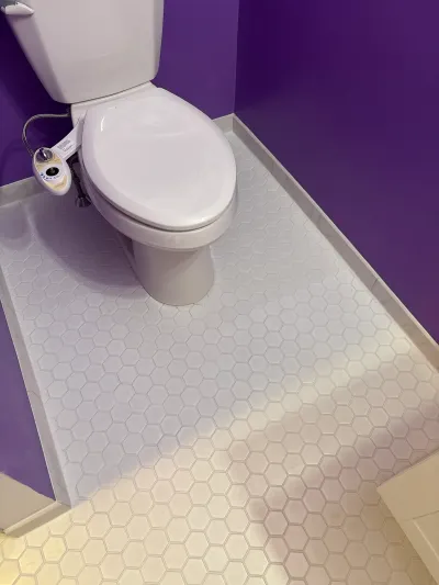 White toilet with a bidet attachment sits on hexagon tile flooring against a purple wall.