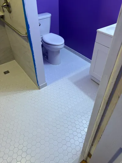 An accessible bathroom remodel in progress with hex tile flooring, a curbless shower, and purple walls.