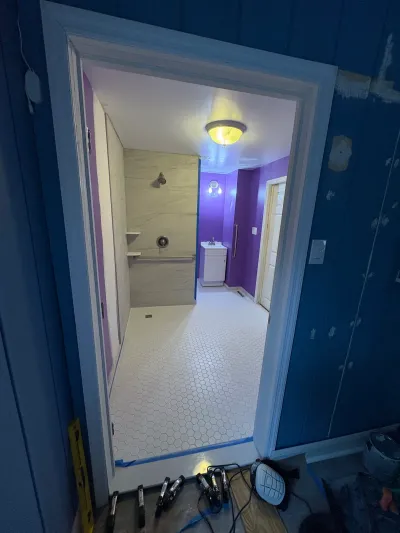 View through a doorway into a bathroom mid-renovation with new tile flooring and a walk-in shower.