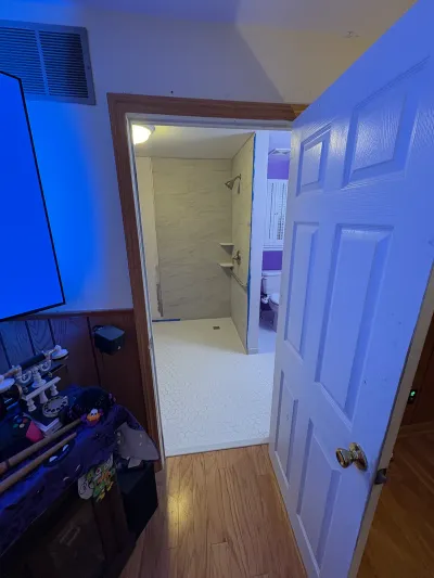 A bathroom renovation in progress with tiled shower walls, hex tile flooring, and painter's tape on trim.