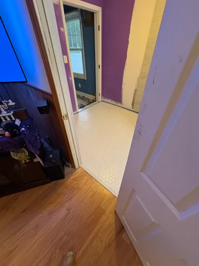 A bathroom mid-renovation with new white hexagon tile flooring and purple walls, seen from a hallway.
