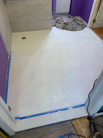 Bathroom floor with new white hexagon tile and grout haze, purple walls, and taped edges during renovation.
