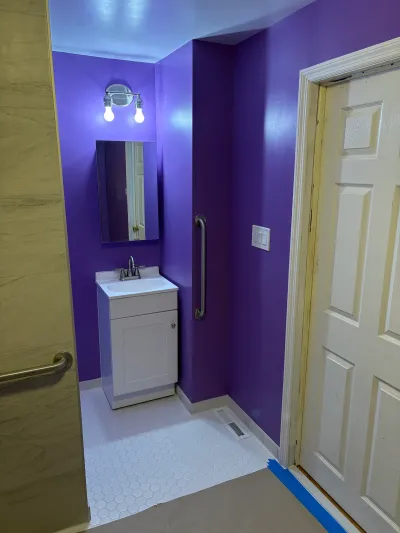 Small bathroom vanity area with purple walls, white hex tile floor, and a grab bar near the door.
