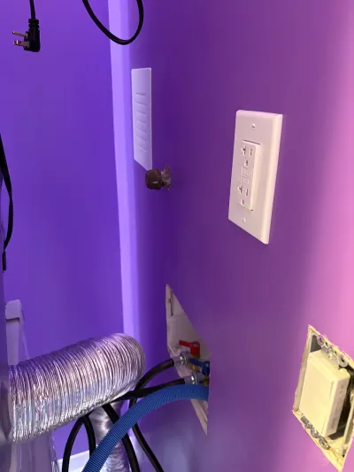 Laundry wall in progress with exposed plumbing valves, dryer duct, and an installed GFCI outlet.