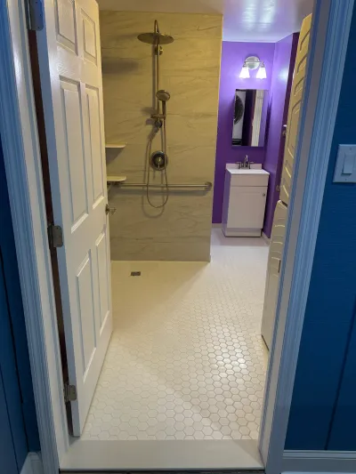 Remodeled bathroom with a curbless tiled shower, grab bar, and adjoining vanity area with purple walls.