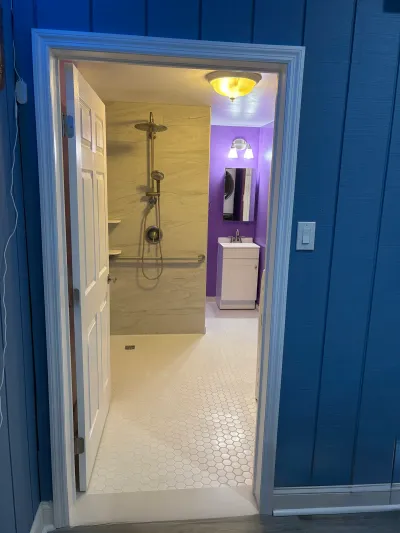 View through a doorway into a renovated bathroom with a curbless tile shower and purple-walled vanity area.