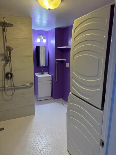 Purple-walled accessible bathroom with a tiled walk-in shower, grab bars, and a white vanity.