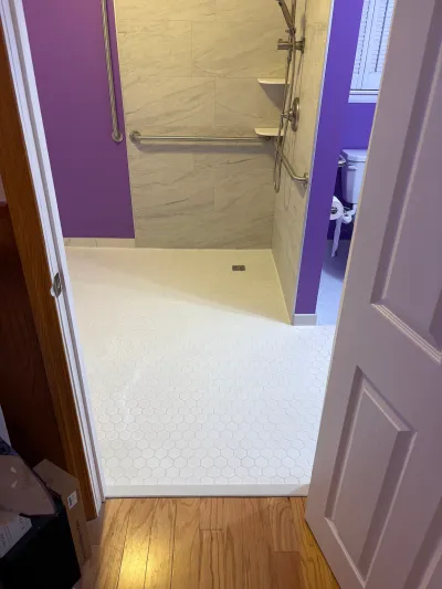 A curbless walk-in shower with hex tile flooring and grab bars, viewed through a doorway.
