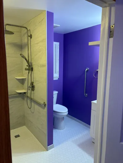 Accessible bathroom with a curbless walk-in shower, grab bars, and a bold purple accent wall.