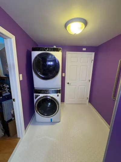 A stacked washer and dryer in a narrow laundry closet with purple walls and hexagon tile flooring.