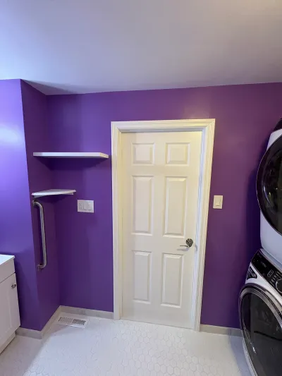 A laundry room with purple walls, hex tile flooring, a white paneled door, and a stacked washer and dryer.