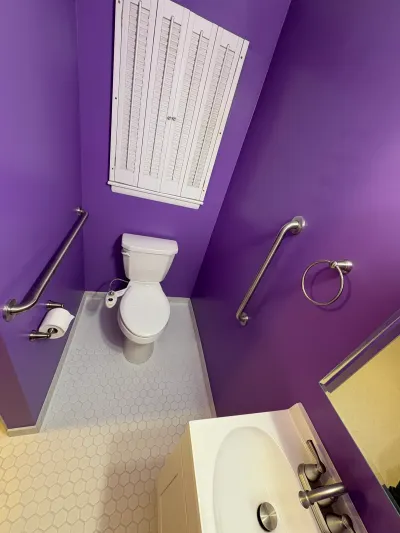 Small purple half bathroom with grab bars, hex tile floor, and a toilet under a sloped ceiling.