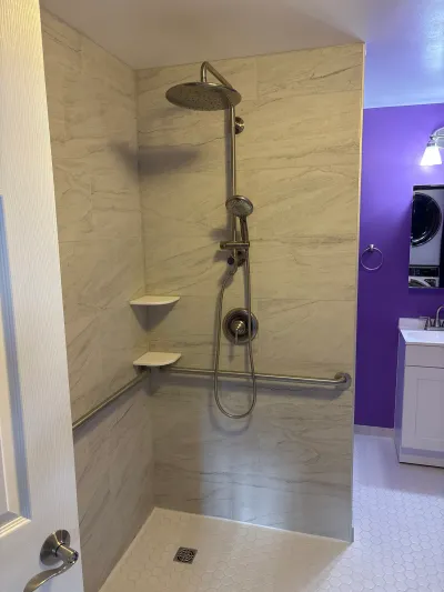 Curbless walk-in shower with marble-look tile, rainfall shower head, and grab bars, opening to a purple-accented bathroom.