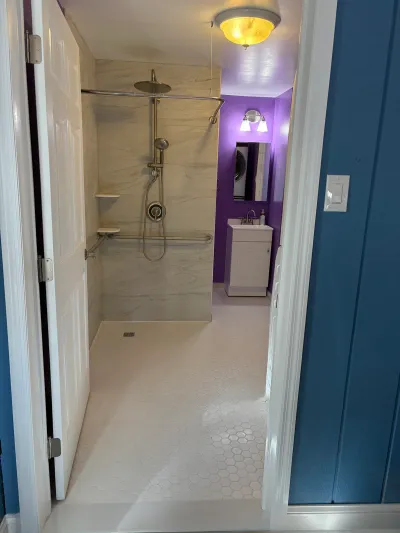 Accessible curbless shower with grab bars leads to a vanity area with a purple accent wall.