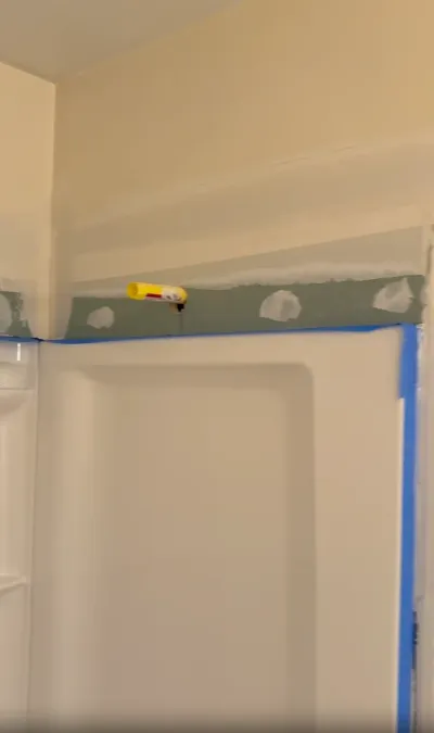 Drywall seam above a shower surround being taped and mudded during a bathroom remodel.