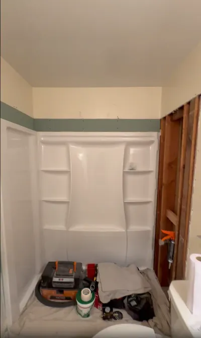 A bathroom shower mid-renovation with a new surround installed and exposed wall studs alongside.