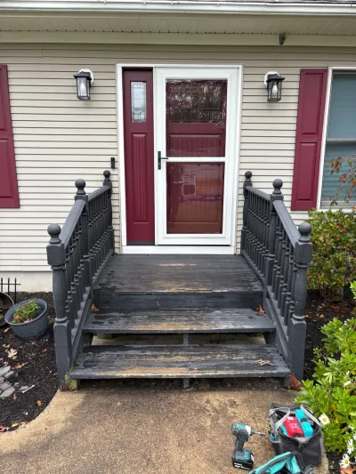 Weathered wooden porch steps with peeling paint below a burgundy front door, tools resting nearby.